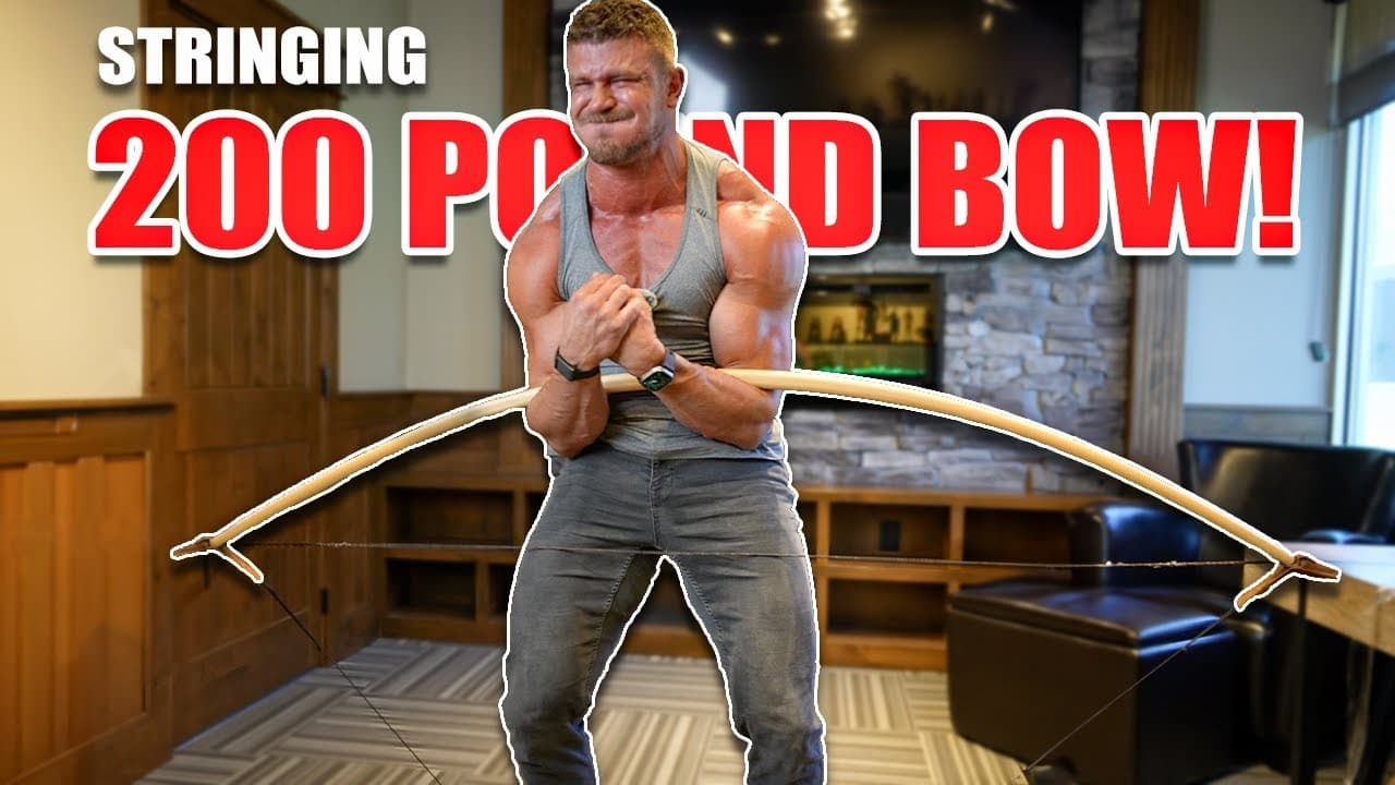 A muscular man in a gray tank top grimacing as he bends a long pale warbow against his body to string it, under the words "Stringing 200 pound bow!"