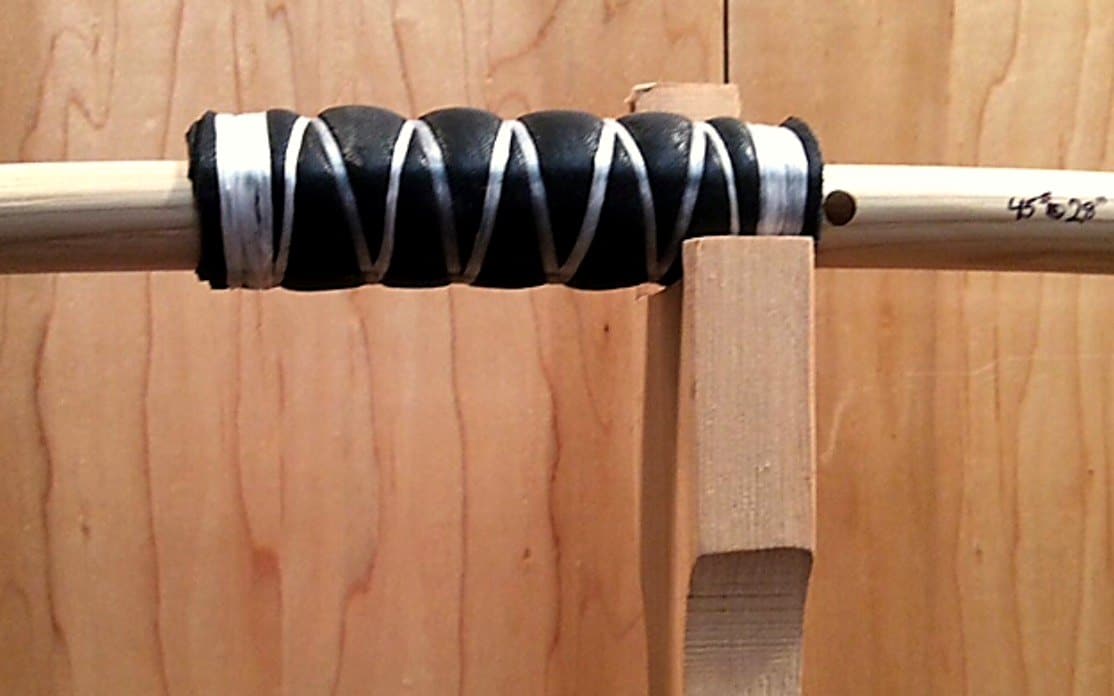 A black leather handle wrap bound with white sinew, the draw weight pencilled on the limb beside it